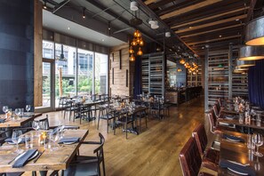 A spacious restaurant with wooden tables and chairs, large windows, and hanging pendant lights. - Kimpton Hotel Palomar Phoenix Cityscape by IHG (Phoenix)