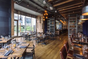 Un restaurante amplio con mesas y sillas de madera, ventanas grandes y lámparas colgantes.