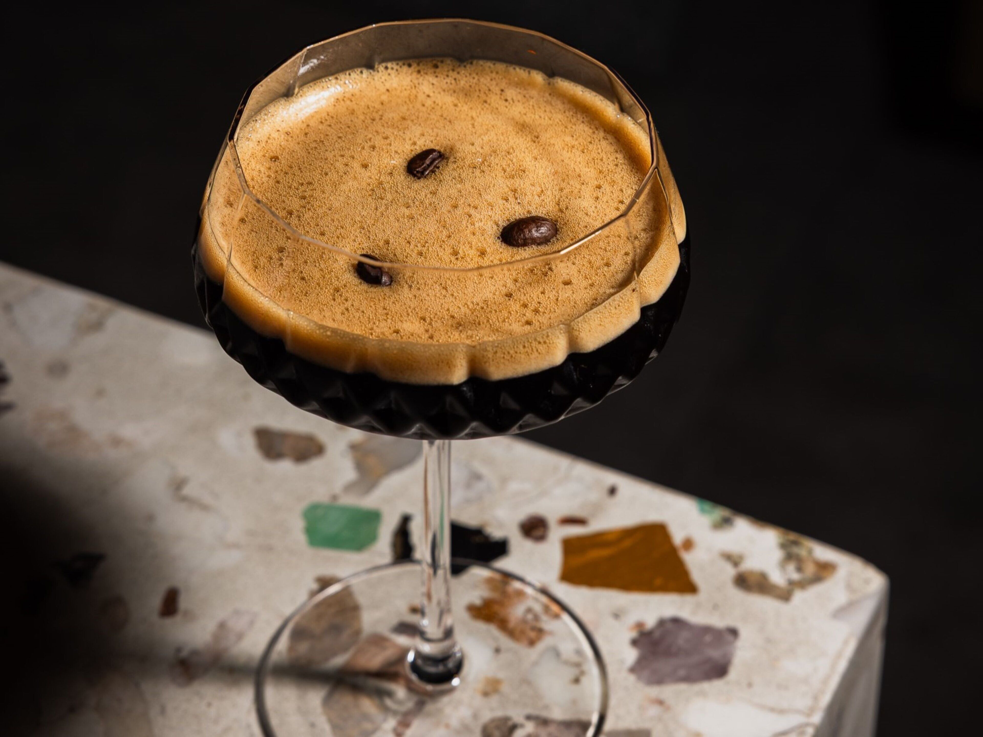 A cocktail in a glass with a decorative rim, placed on a marble surface with colorful stains.