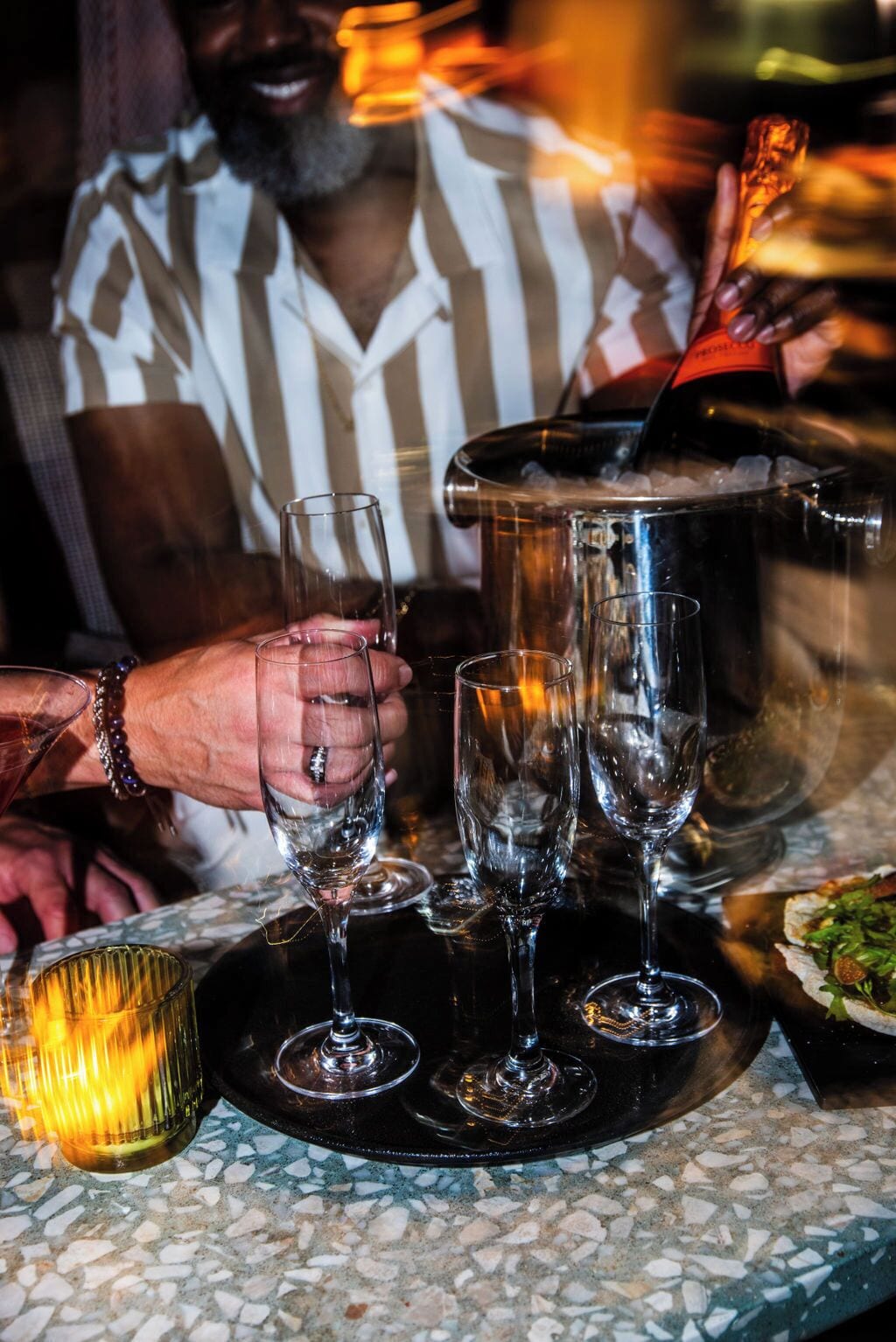 Un coin bar avec un seau en métal, plusieurs verres et une bougie sur une table.