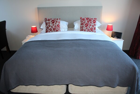 A neatly made bed with a grey and white checkered bedspread, two red and white patterned pillows, and two bedside lamps with red shades. - Chalet Queenstown (Queenstown)