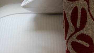 A bed with white bedding and a red and beige patterned pillow.