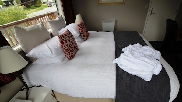 Una cama bien hecha con ropa blanca y almohadas rojas estampadas, una toalla blanca doblada y una lámpara de noche.