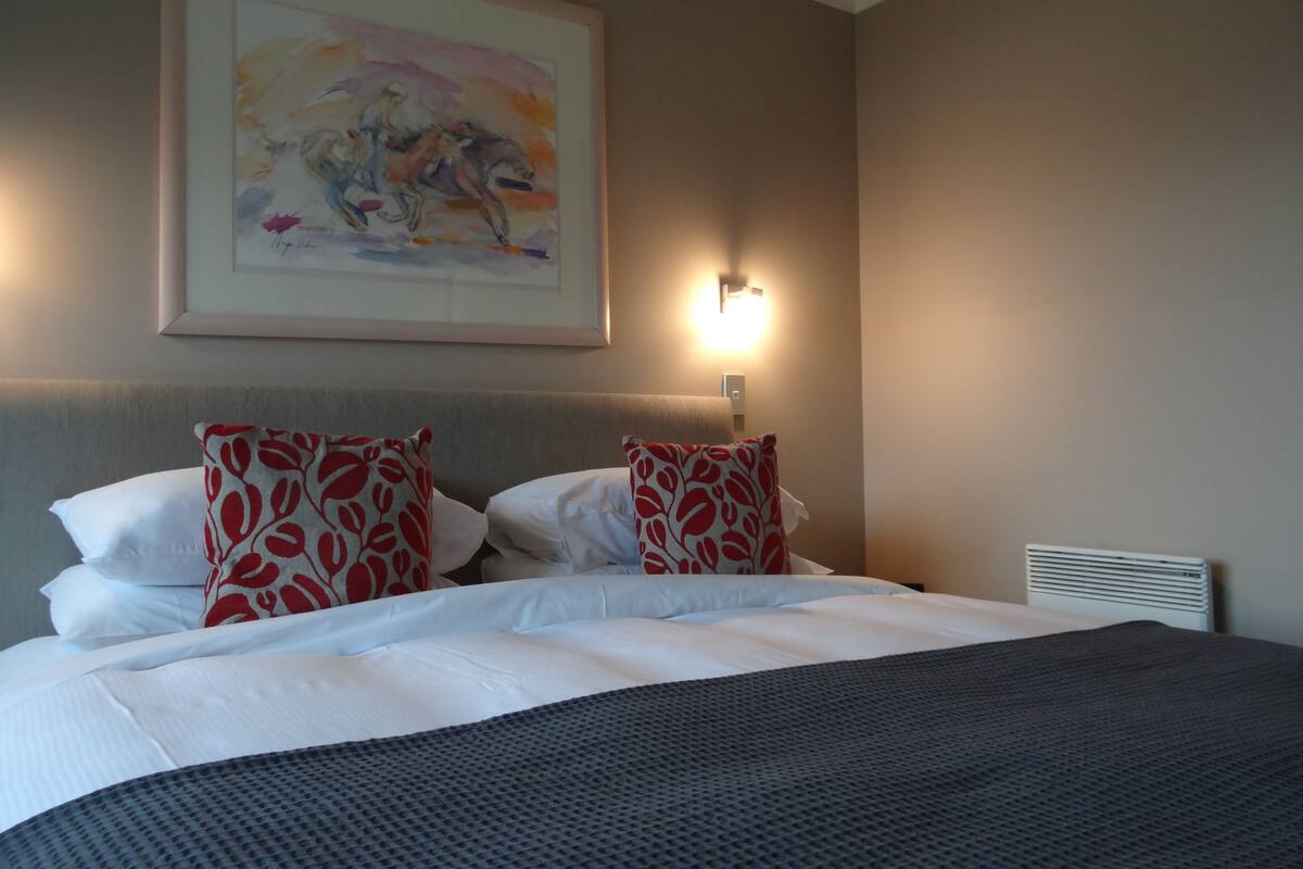 Una habitación de hotel con cama, almohadas, una lámpara de pared y un cuadro.