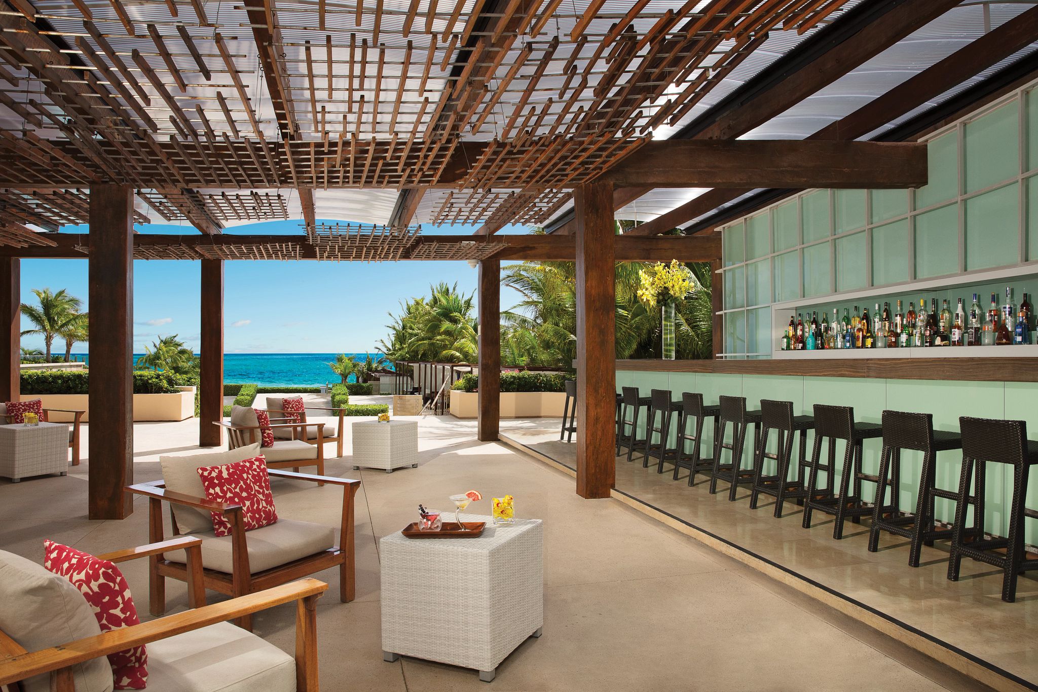 An outdoor seating area with a view of the ocean, a bar with a variety of bottles, and a pergola structure.