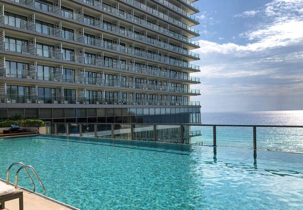 A high-rise hotel with a large infinity pool overlooking the ocean. - Secrets The Vine Cancun - Adults Only - All Inclusive (Cancun)