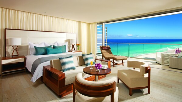 A hotel room with a large bed, a balcony with a view of the ocean, and a seating area with a coffee table.