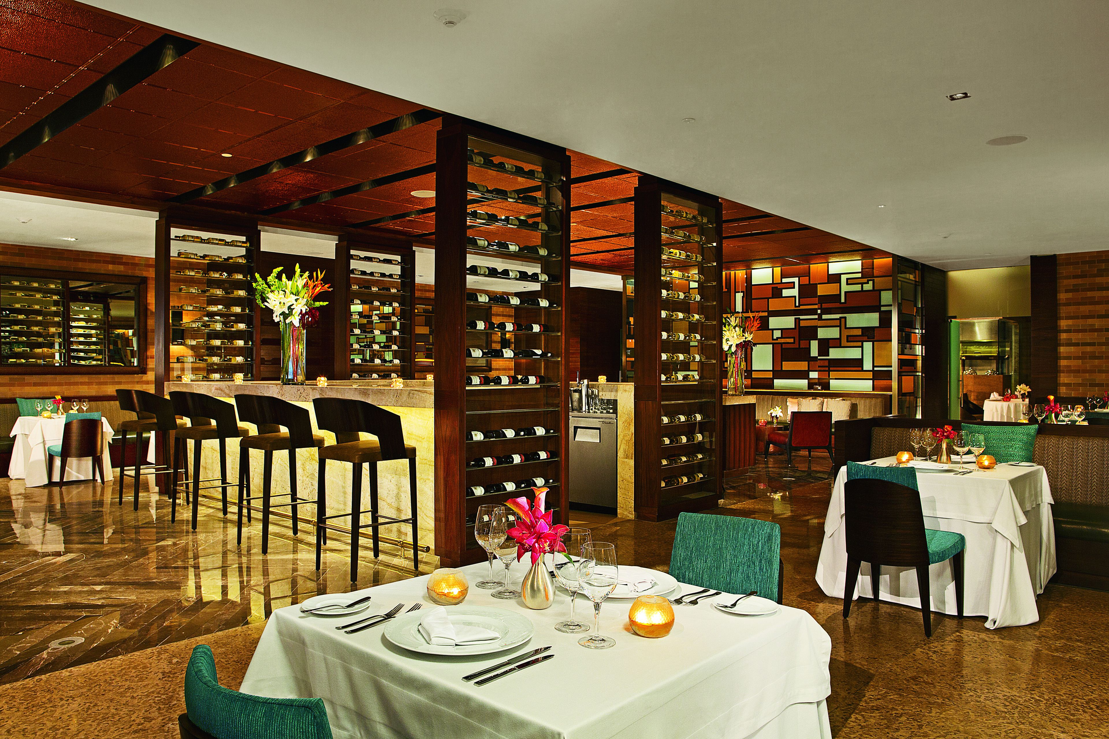 A restaurant with a bar area, multiple tables set for dining, and a wine display.