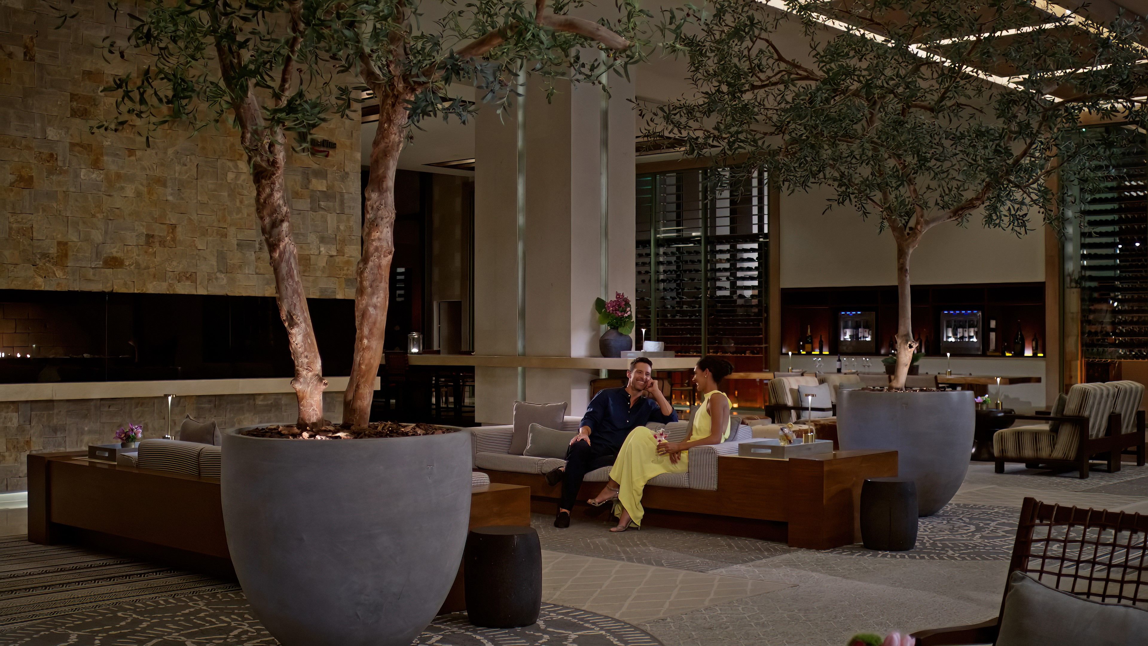 A spacious lobby with large planters, a seating area, and a wine rack in the background.