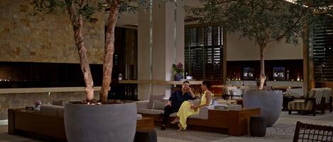 A spacious lobby with large planters, a seating area, and a wine rack in the background.
