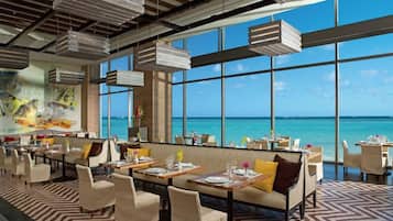 Un restaurante con vistas al mar, que cuenta con techos altos, lámparas colgantes y un suelo estampado.
