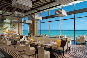 Un restaurante con vistas al mar, que cuenta con techos altos, lámparas colgantes y un suelo estampado.