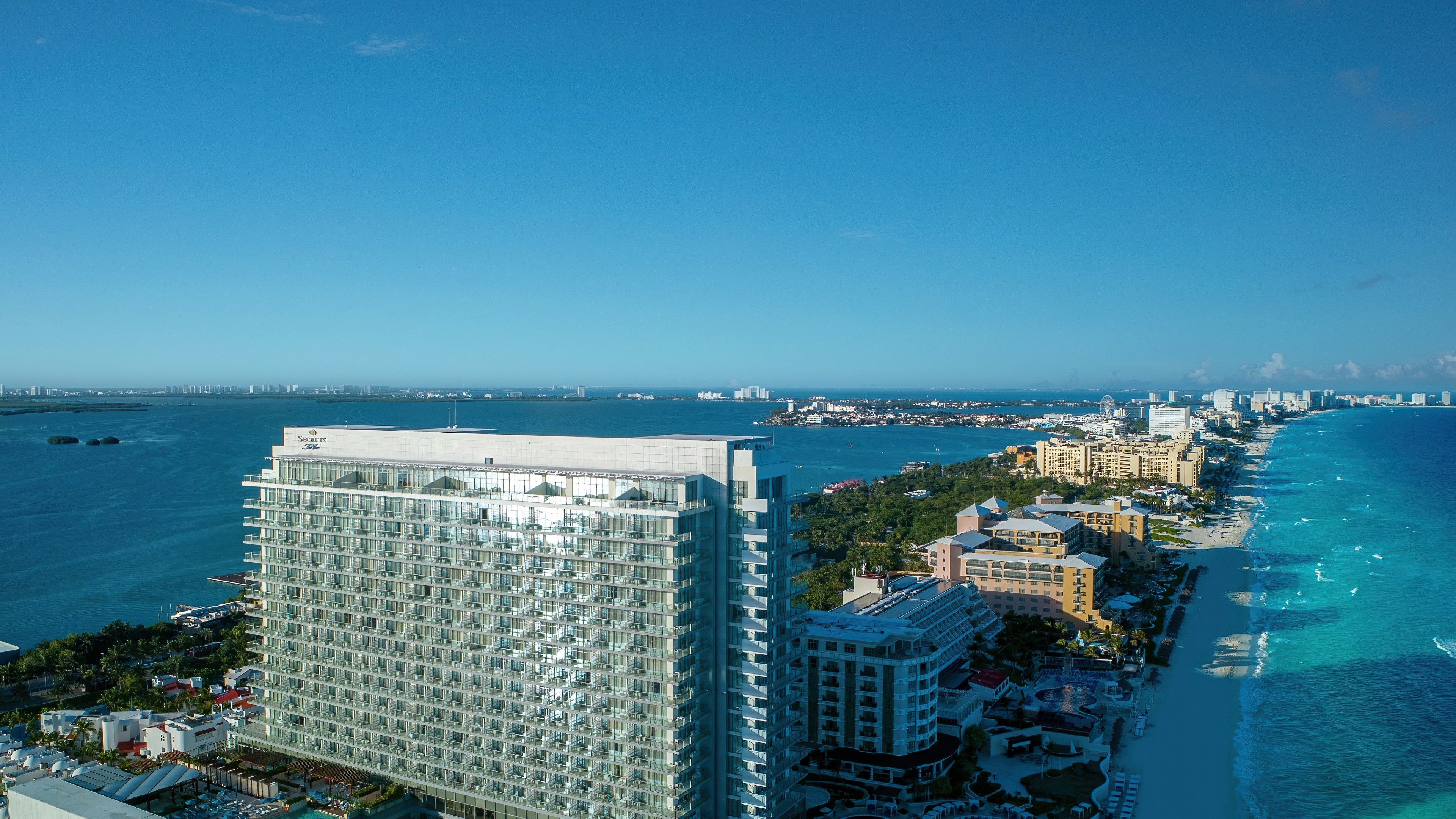 A high-rise hotel with a modern glass facade, located adjacent to a beach with clear blue waters.