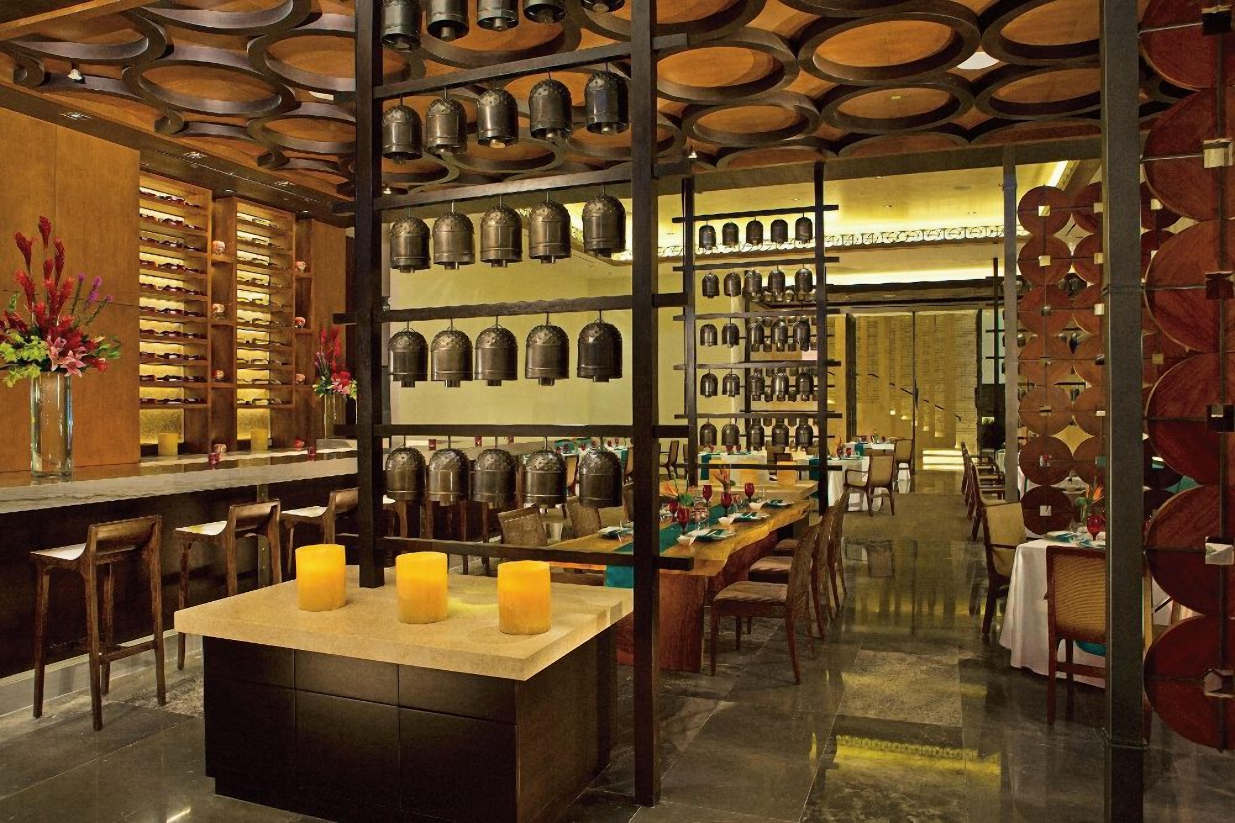 A restaurant interior with a bar area, candlelit tables, and a wall of hanging bells.
