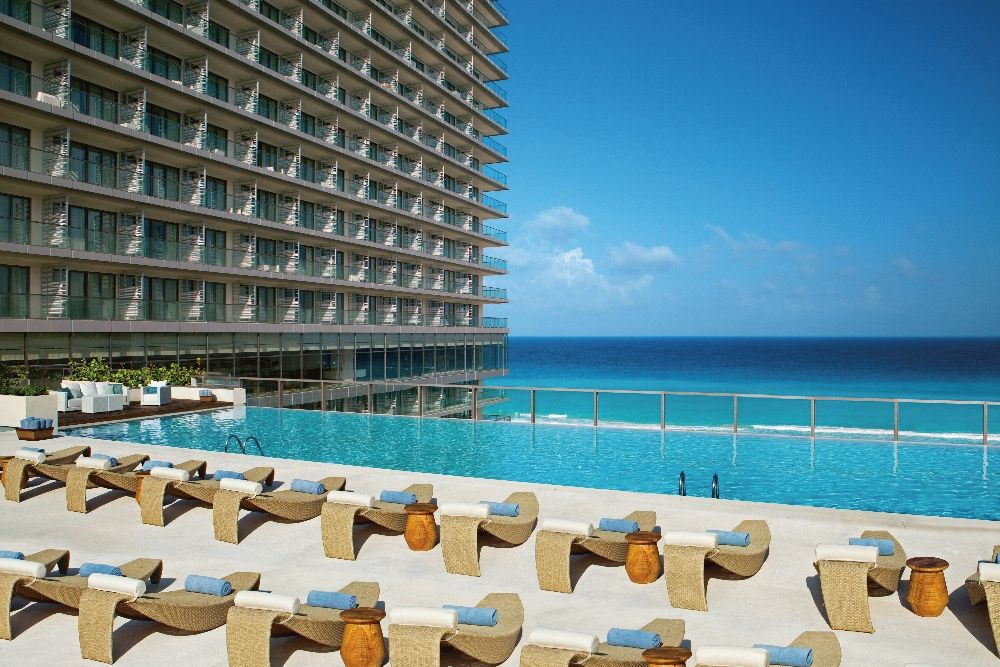 A hotel with a pool overlooking the ocean, lounge chairs, and a high-rise building.