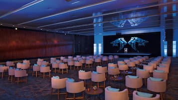 A conference room with rows of chairs, a large screen, and a stage.
