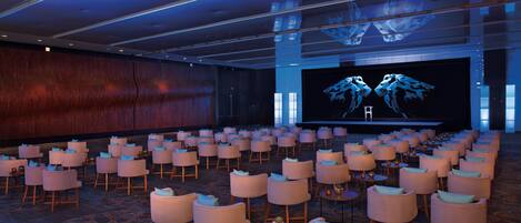 A conference room with rows of chairs, a large screen, and a stage.