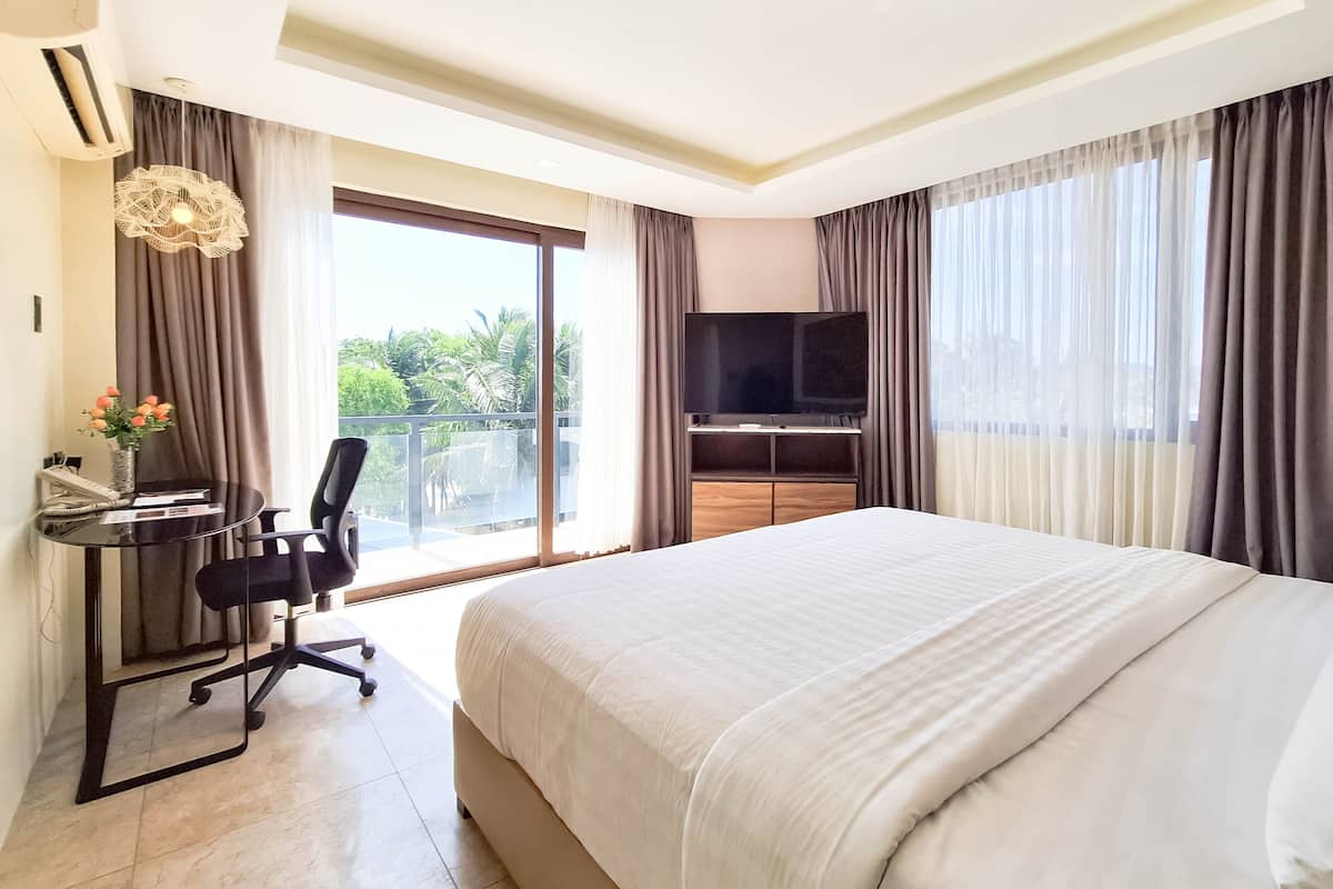 Ein Hotelzimmer mit einem großen Bett, einem Schreibtisch mit Stuhl, einem Flachbildfernseher und einem Balkon mit Vorhängen.