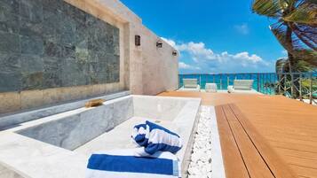 A pool area with a wooden deck, a stone wall, and a clear view of the ocean.