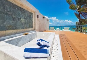 Zona de piscina con muelle de madera, pared de piedra y vista despejada al océano.