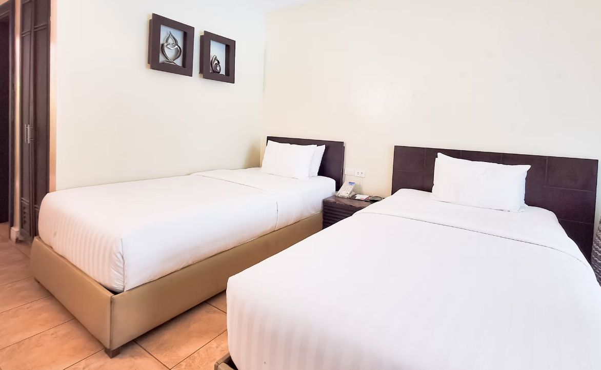 A hotel room with two single beds, a bedside table with a phone, and two framed pictures on the wall.