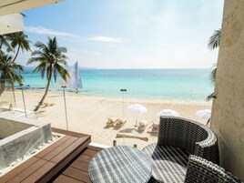 A beach view from a balcony with a wooden deck, lounge chairs, and umbrellas.