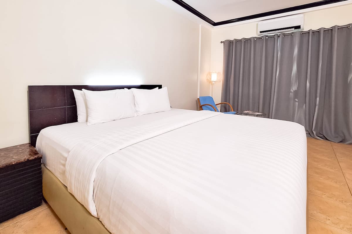 Ein Hotelzimmer mit einem großen Bett, einem Sessel, einem Nachttisch und einer Wand-Klimaanlage.