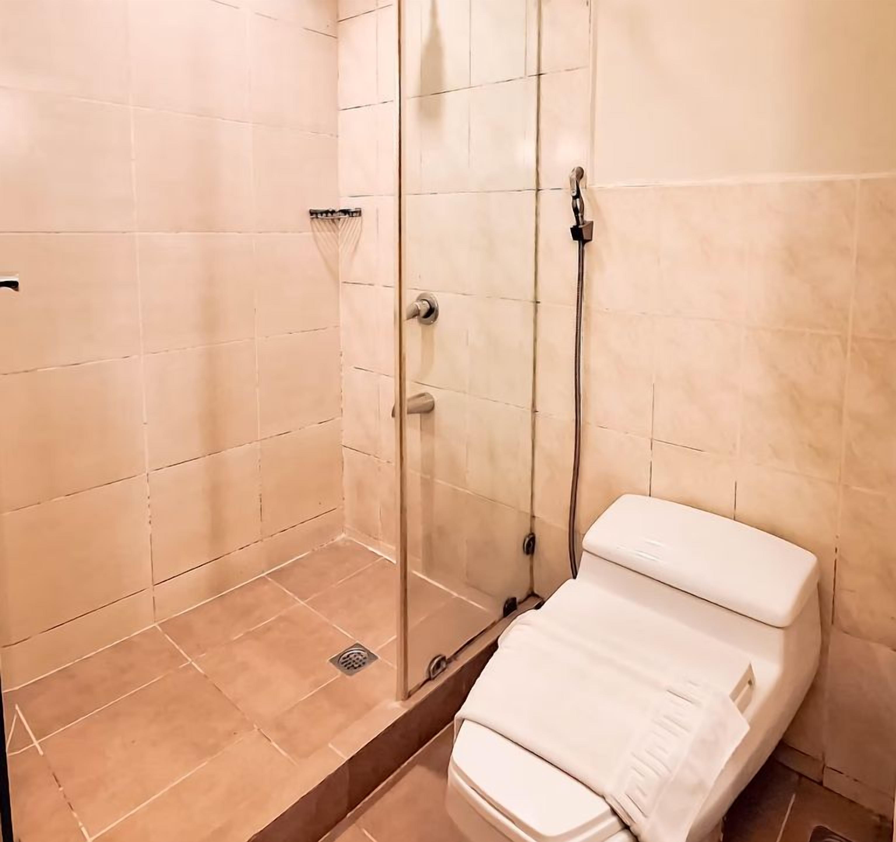 A shower with a glass door, a handheld showerhead, and a white towel on the floor.