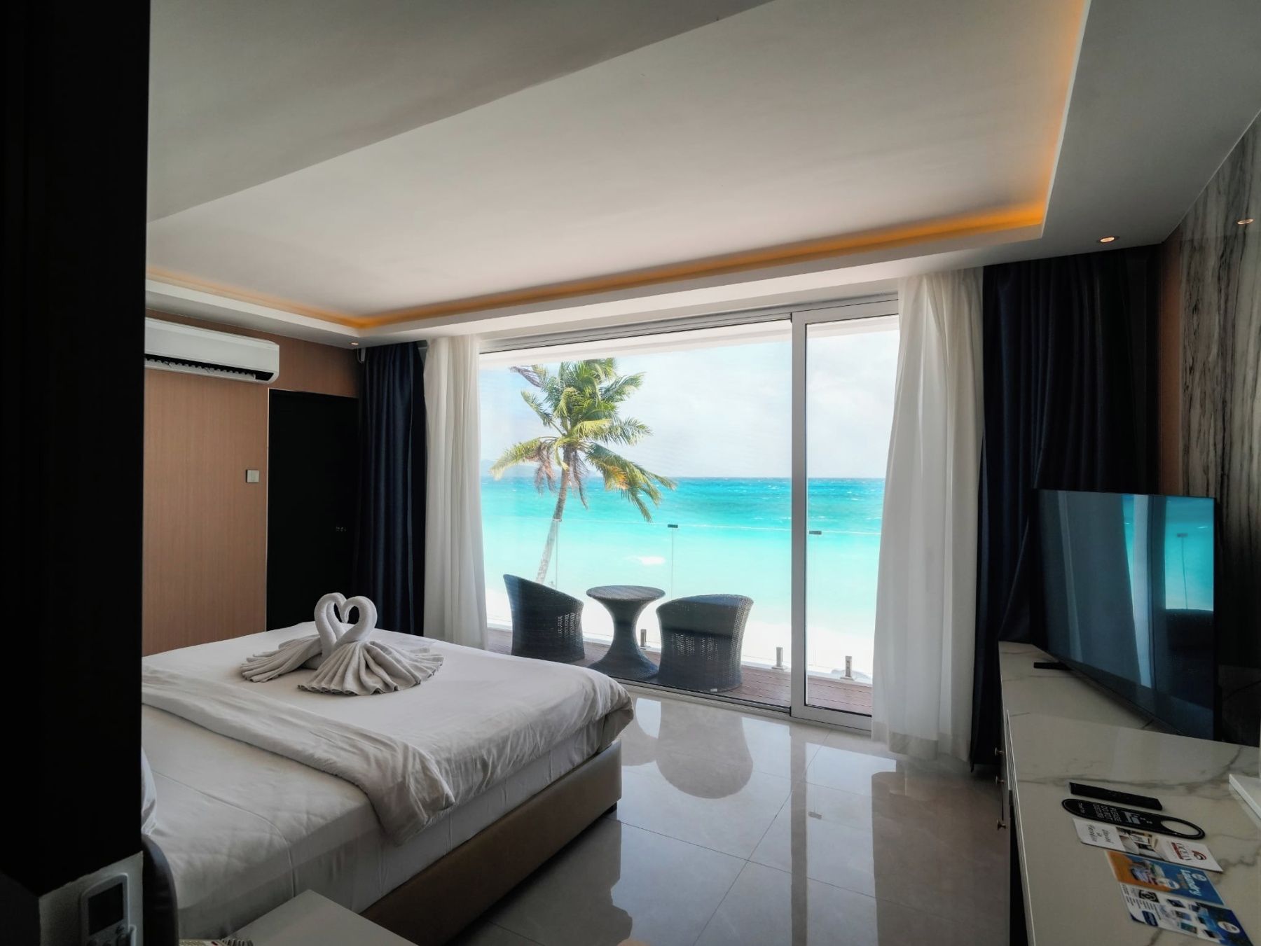 A hotel room with a bed, a TV, a desk, and a view of the ocean.