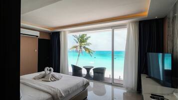 A hotel room with a bed, a TV, a desk, and a view of the ocean.
