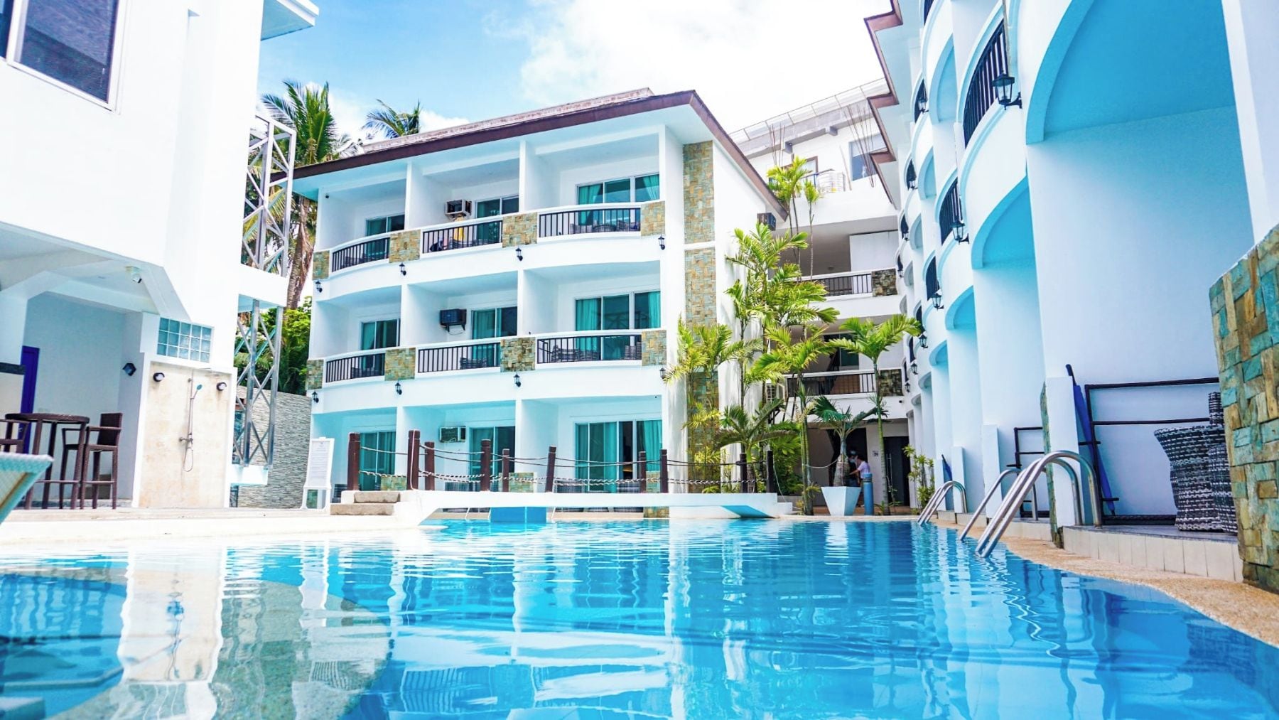 Un hotel con piscina, varios balcones y cielo despejado.