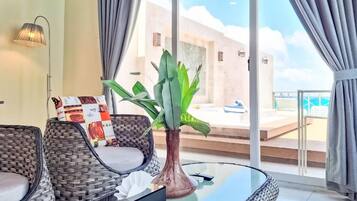 A modern room with wicker furniture, a glass table, and a view of a pool and building.