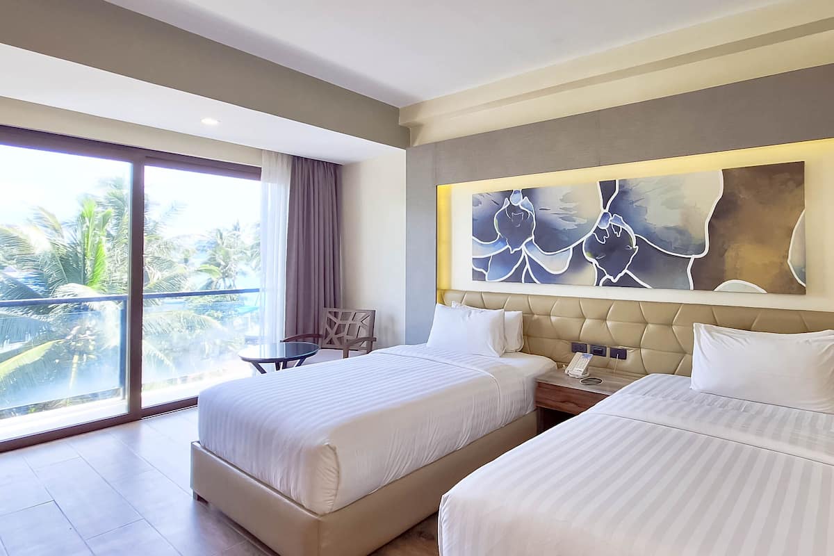 Ein Hotelzimmer mit zwei Betten, einem großen Fenster mit Blick auf Palmen und einem modernen, abstrakten Gemälde an der Wand.