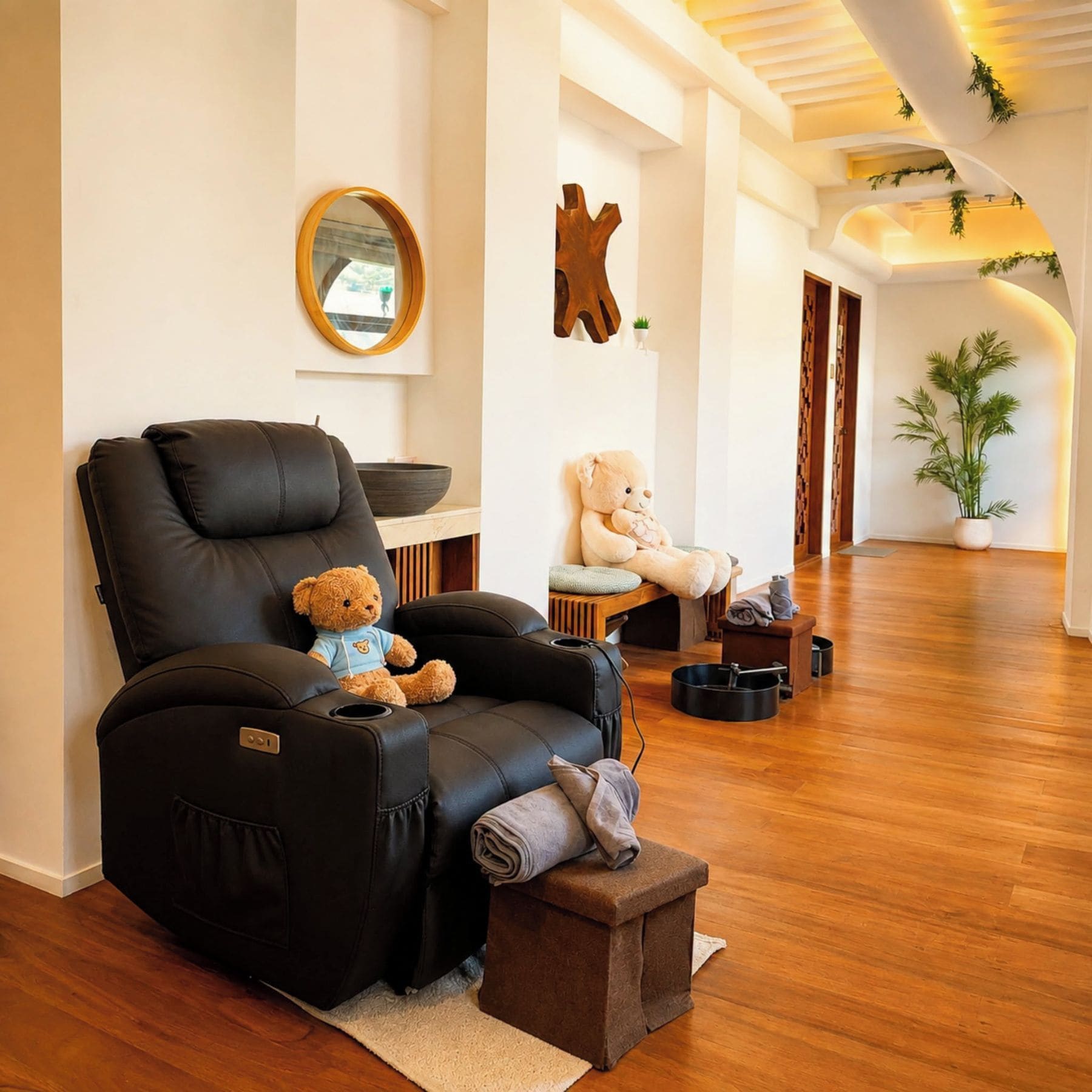 Una silla de masaje con un oso de peluche, un banco de madera con otro oso de peluche y una planta en maceta en un salón moderno.