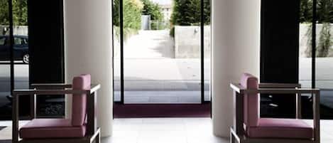 A modern entrance with two pink chairs and a glass door leading outside.