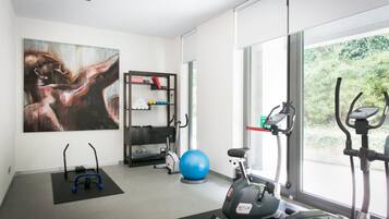 A modern gym with exercise equipment, a large abstract painting, and a view of greenery through large windows.