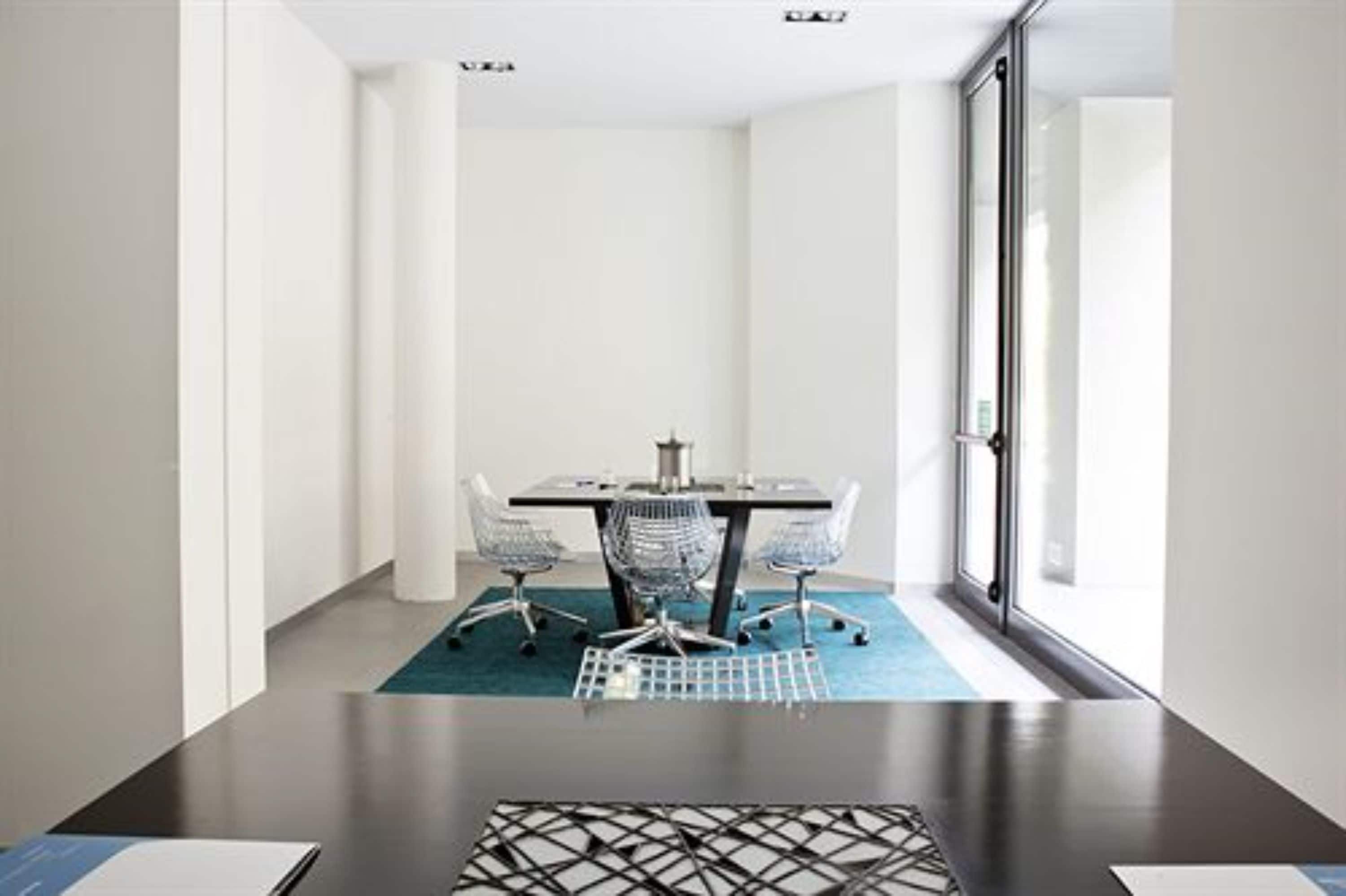 A conference room with a dark wooden table, four office chairs, and a blue carpet.