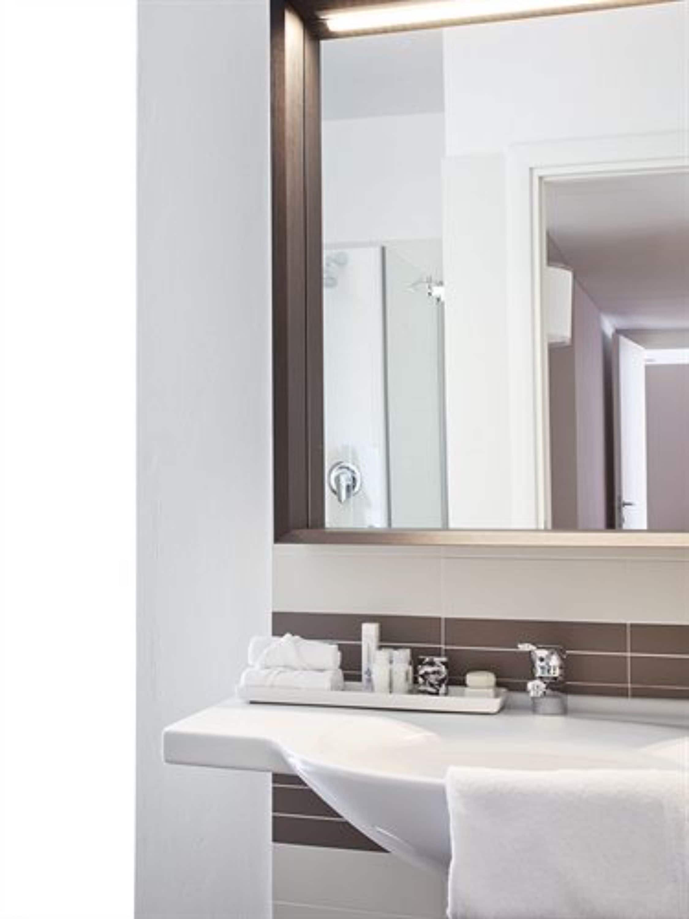 A modern bathroom with a large mirror, a white sink, and a towel rack.