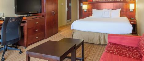 A hotel room with a bed, a desk with a computer, a TV, and a red sofa.