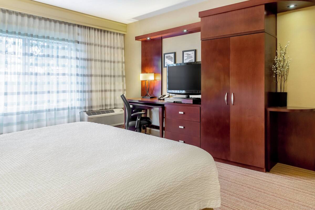 Una habitación de hotel con una cama grande, un escritorio con silla, un televisor y un armario.