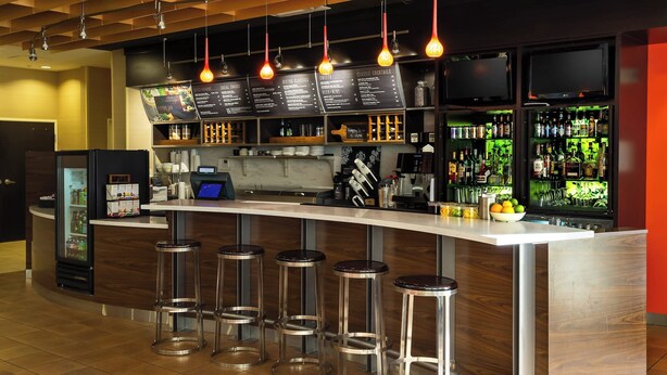 Un espace bar comprenant un tableau affichant le menu, des tabourets, un réfrigérateur et un comptoir.