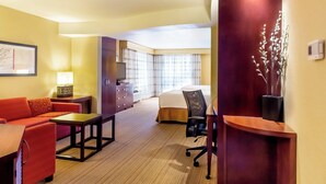 Une chambre d’hôtel comprenant un canapé, une petite table, un bureau, une chaise, un lit, une fenêtre avec des rideaux et un climatiseur fixé au mur.
