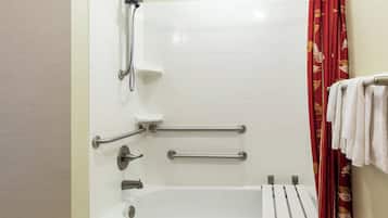 A bathroom with a white bathtub, grab bars, a showerhead, and a red floral curtain.