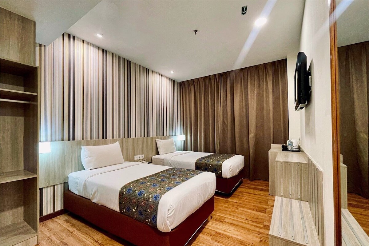 A hotel room with two beds, wooden flooring, striped curtains, a flat-screen TV, and a small table with a coffee maker.