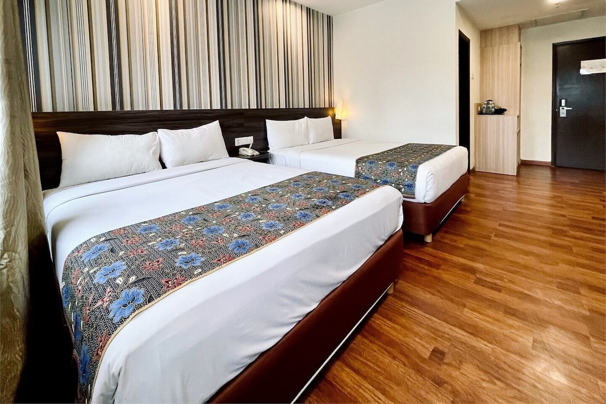 A hotel room with two beds, a wooden floor, and a striped wall.