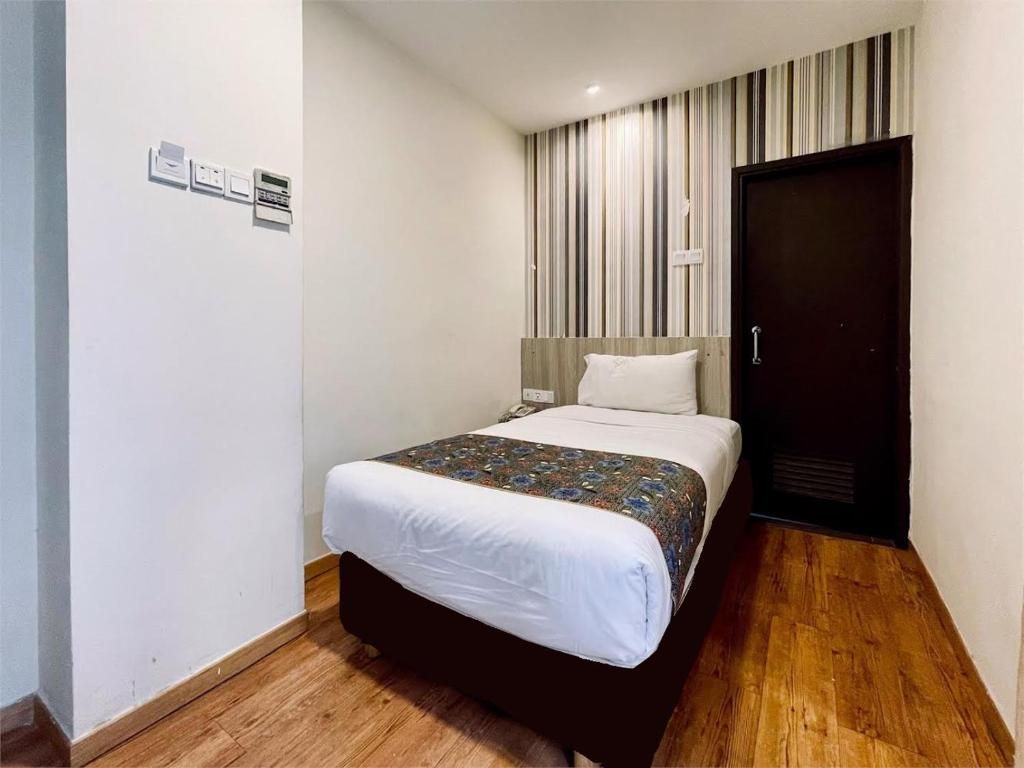 Une chambre d’hôtel avec un lit, un plancher en bois, une porte sombre et un rideau à rayures.