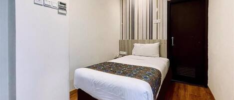 A hotel room with a bed, a wooden floor, a dark door, and a striped curtain.