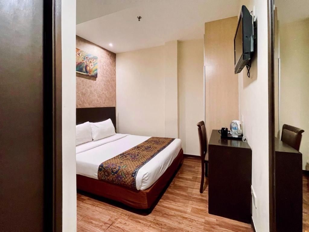 A hotel room with a bed, a desk, a chair, and a television.