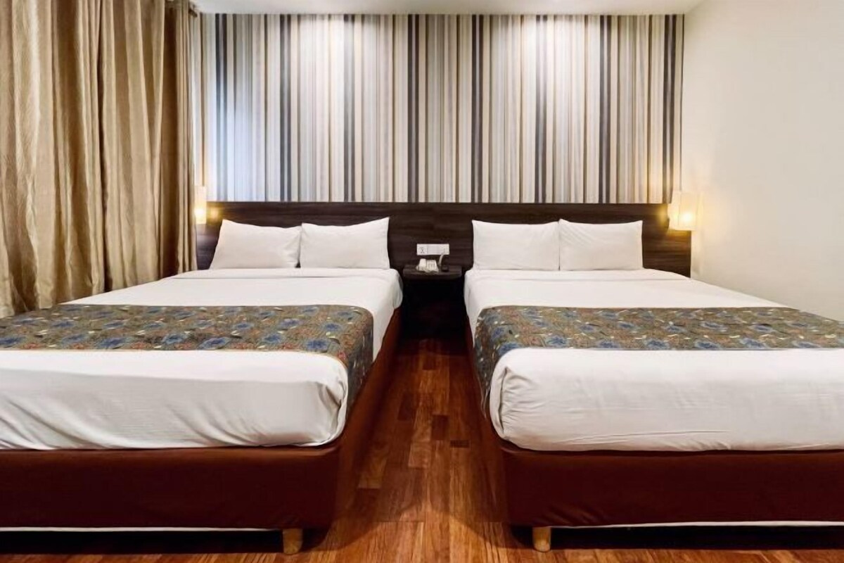 A hotel room with two beds, a wooden floor, a striped curtain, and a nightstand with a lamp.