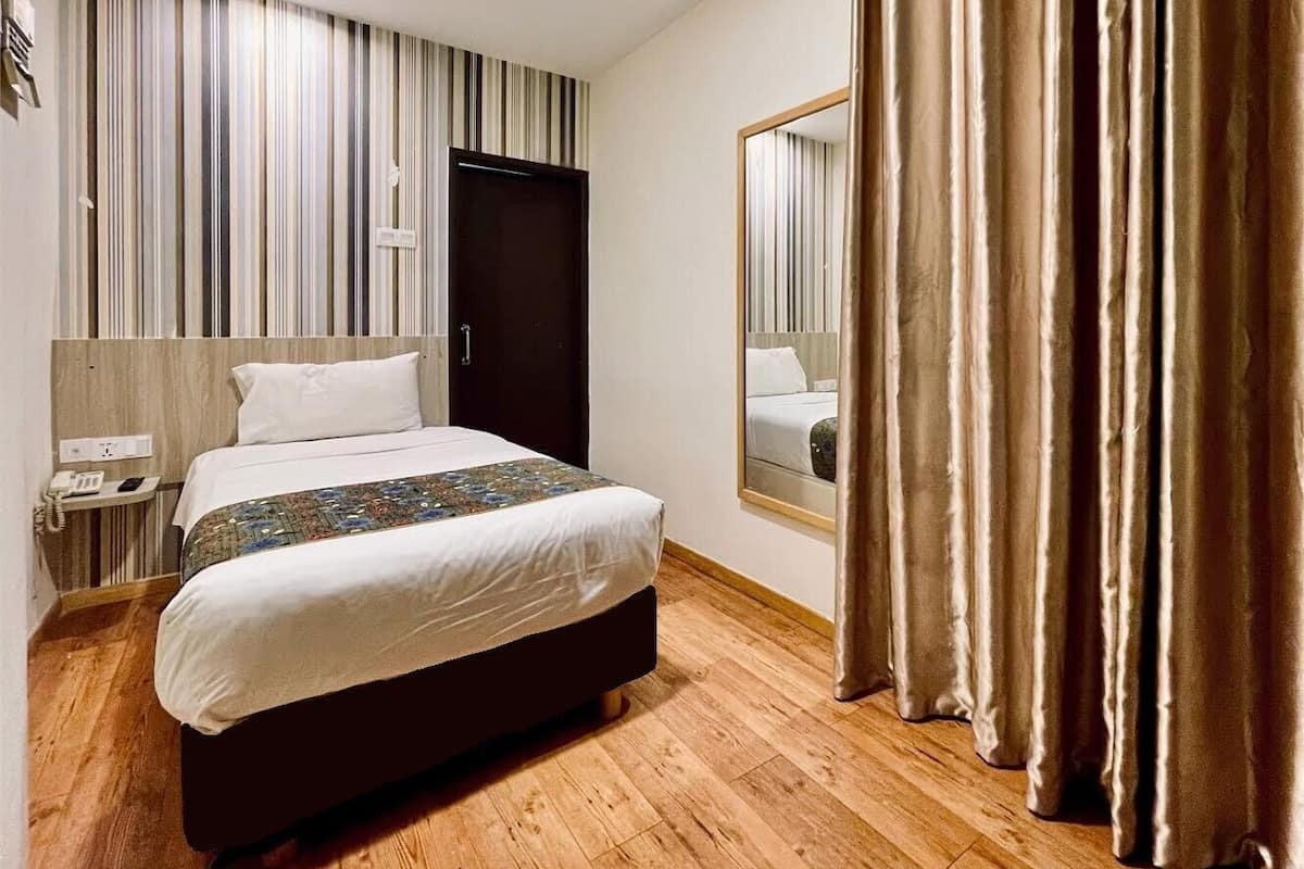 A hotel room with a bed, a nightstand, a mirror, and a curtain.